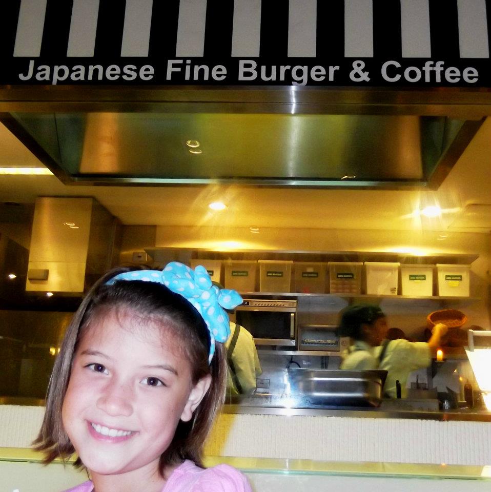 Young girl smiling in front of Mos Burger, a Japanese fast-food chain known for its unique rice burgers.