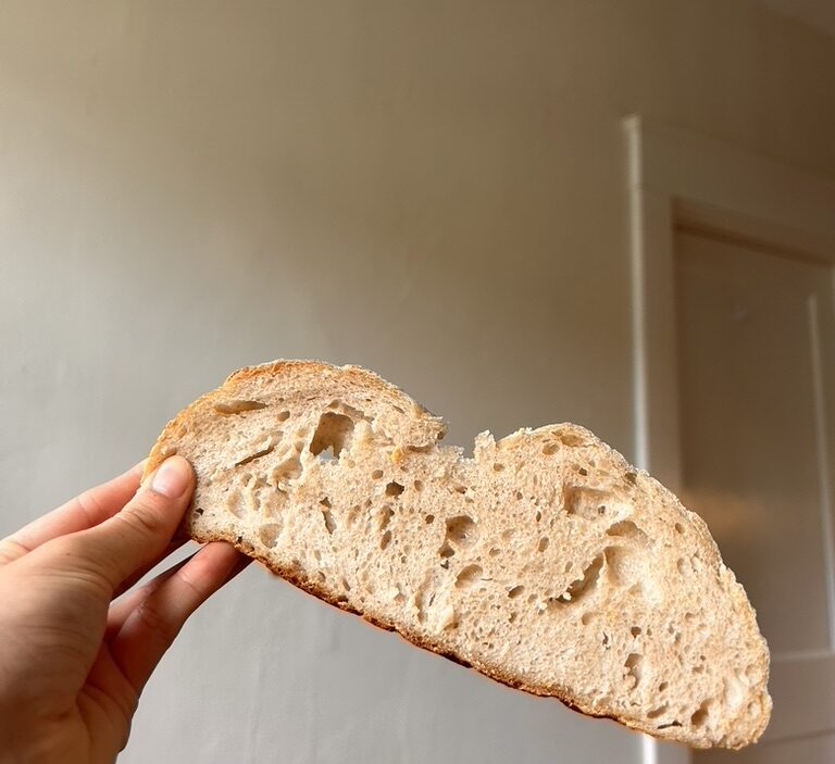 Close-up of a pumpkin-shaped sourdough loaf with leaf-like score details and a cinnamon stick stem.