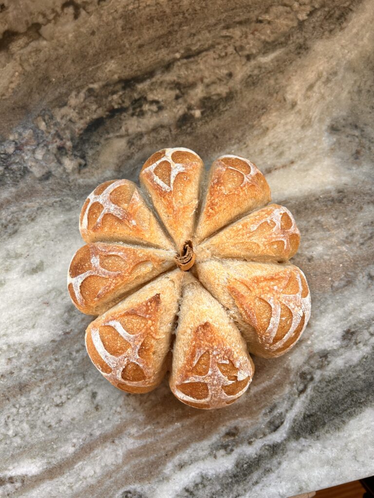 A beautifully crafted sourdough loaf shaped like a pumpkin, with a golden crust and a decorative score design.