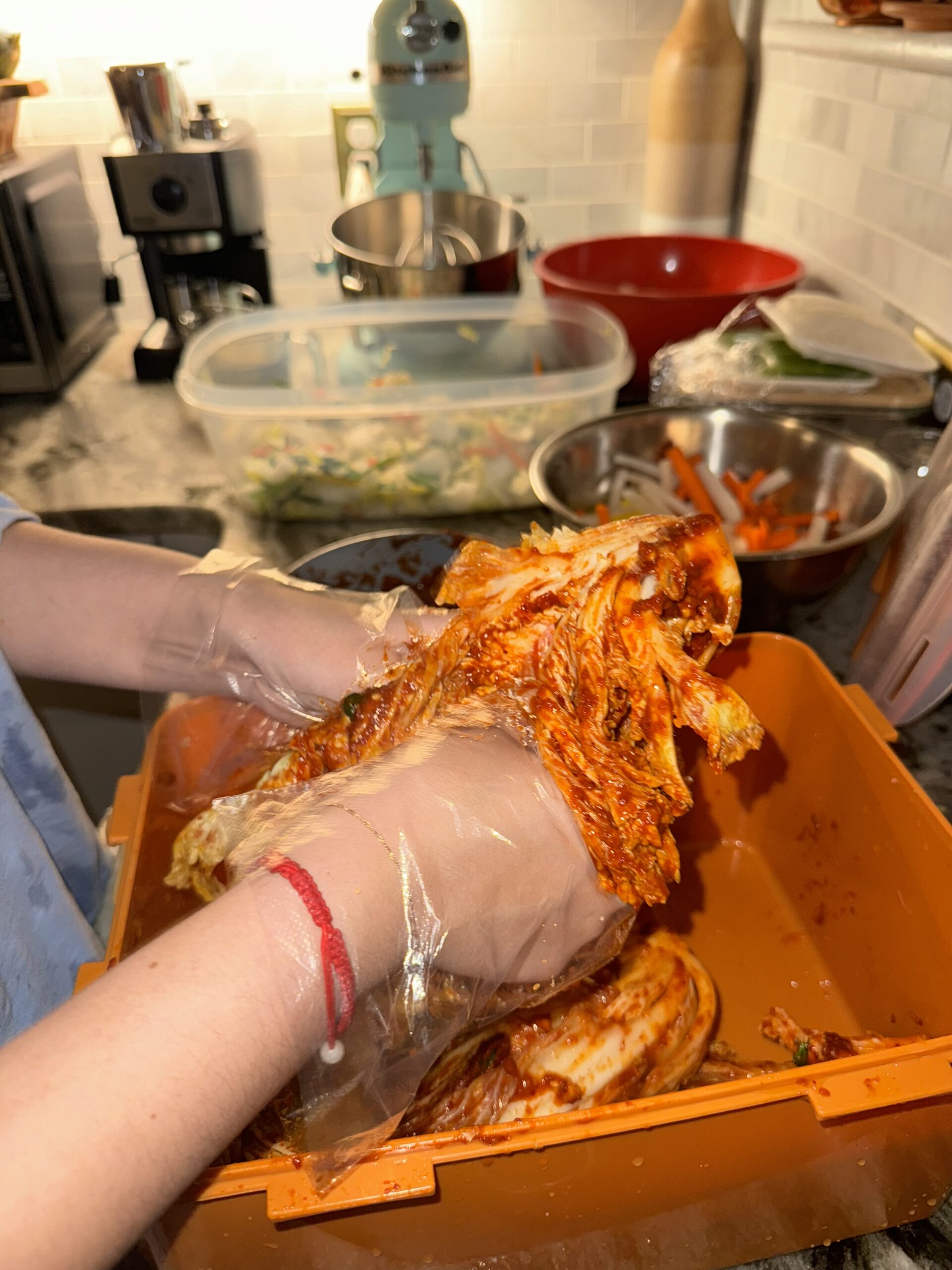 Hands wearing gloves, thoroughly mixing the kimchi paste into the Napa cabbage, showcasing the traditional technique.