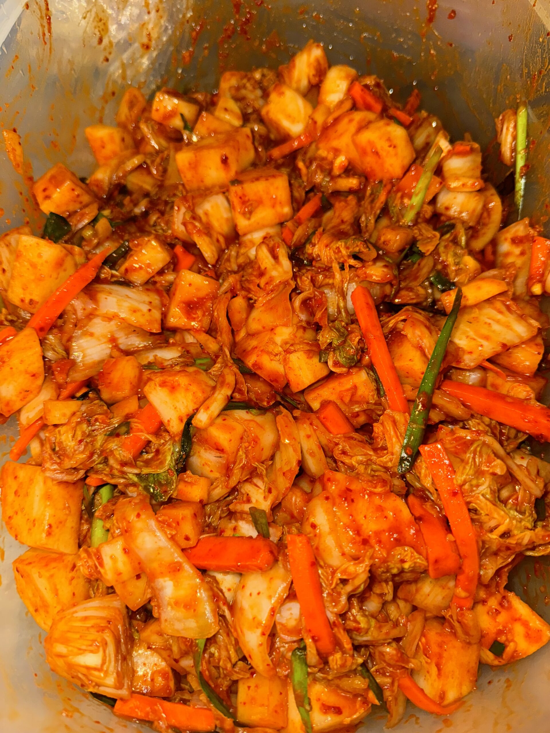 A close-up shot of freshly mixed kimchi, vibrant with julienned carrots, daikon radish, and Napa cabbage coated in red chili paste.