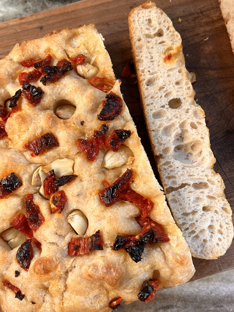 A view of the sundried tomato and garlic focaccia sliced, ready to serve. A close-up of the airy crumb inside the focaccia, showcasing its fluffy texture. A perfectly baked focaccia loaf with sundried tomatoes and garlic, golden and inviting.