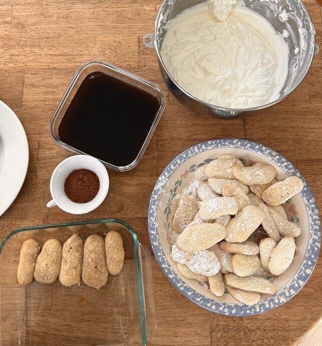 A cozy setup with ingredients for homemade tiramisu, including coffee-soaked ladyfingers, whipped cream, and cocoa powder.