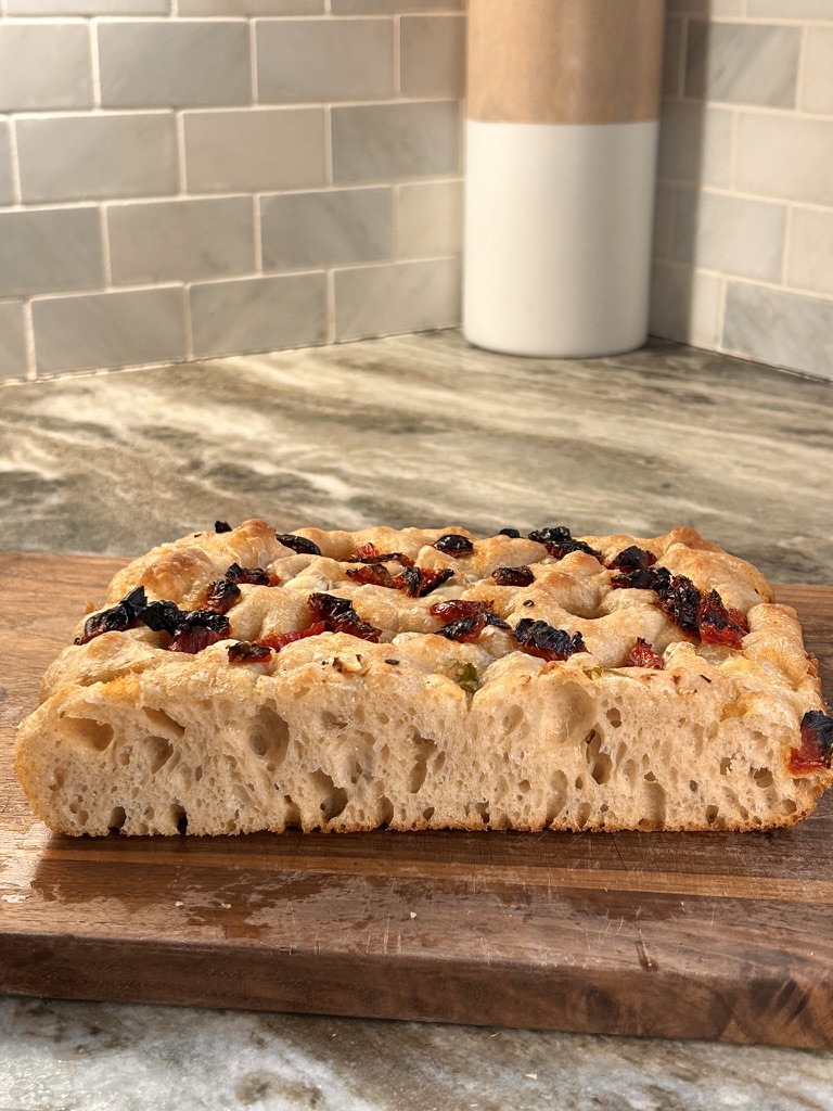 perfectly baked focaccia loaf with sundried tomatoes and garlic, golden and inviting. A view of the sundried tomato and garlic focaccia sliced, ready to serve. A close-up of the airy crumb inside the focaccia, showcasing its fluffy texture. A perfectly baked focaccia loaf with sundried tomatoes and garlic, golden and inviting