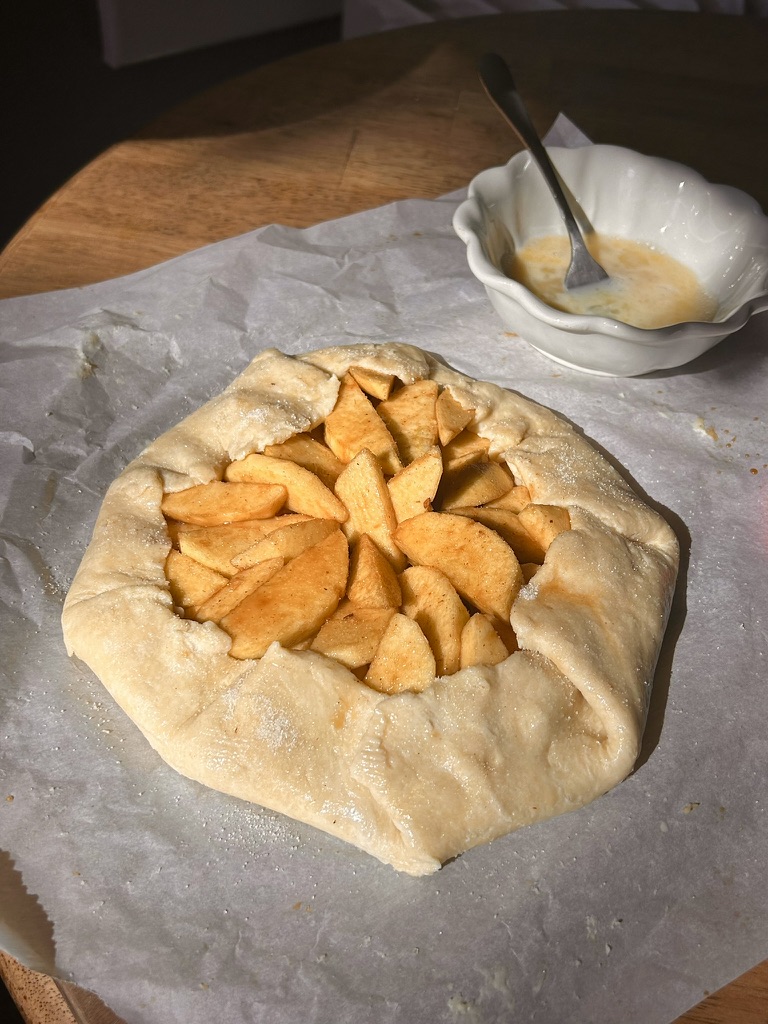 Unbaked apple galette on parchment paper with egg wash in a small bowl nearby.