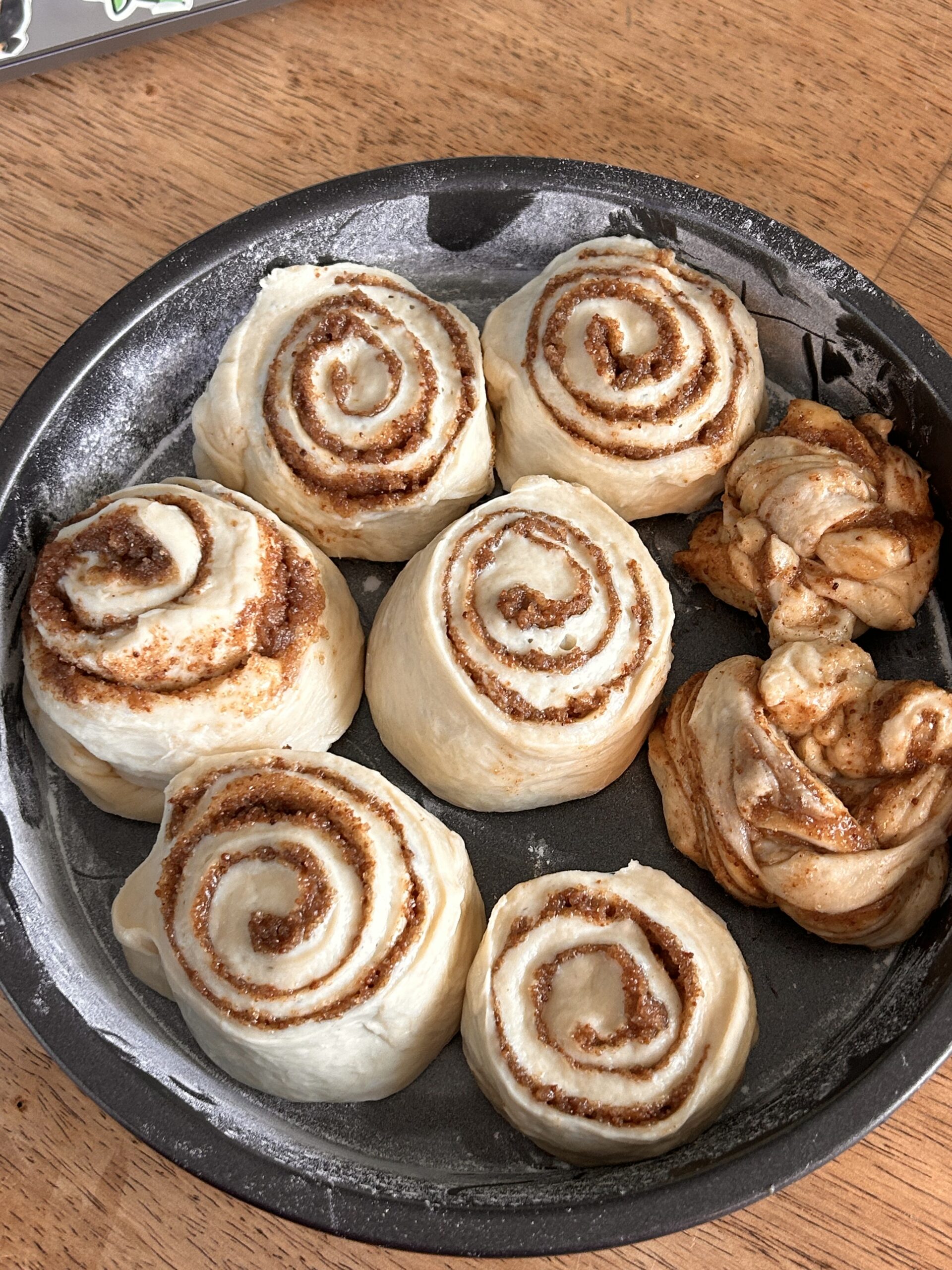 Six unbaked cinnamon rolls in a round pan, perfectly swirled, next to a braided cinnamon twist.