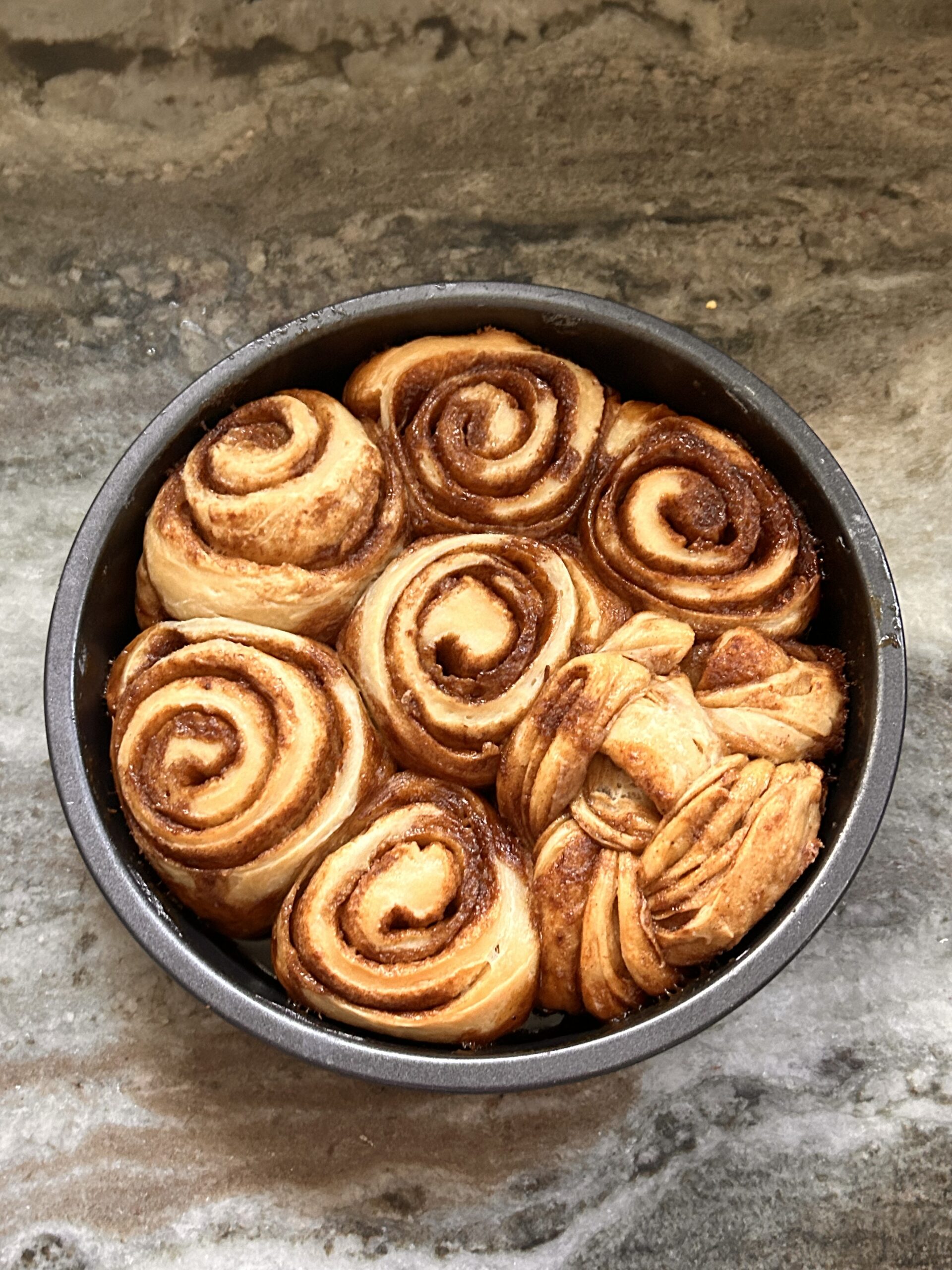 Freshly baked cinnamon rolls in a round pan, golden brown with caramelized edges.