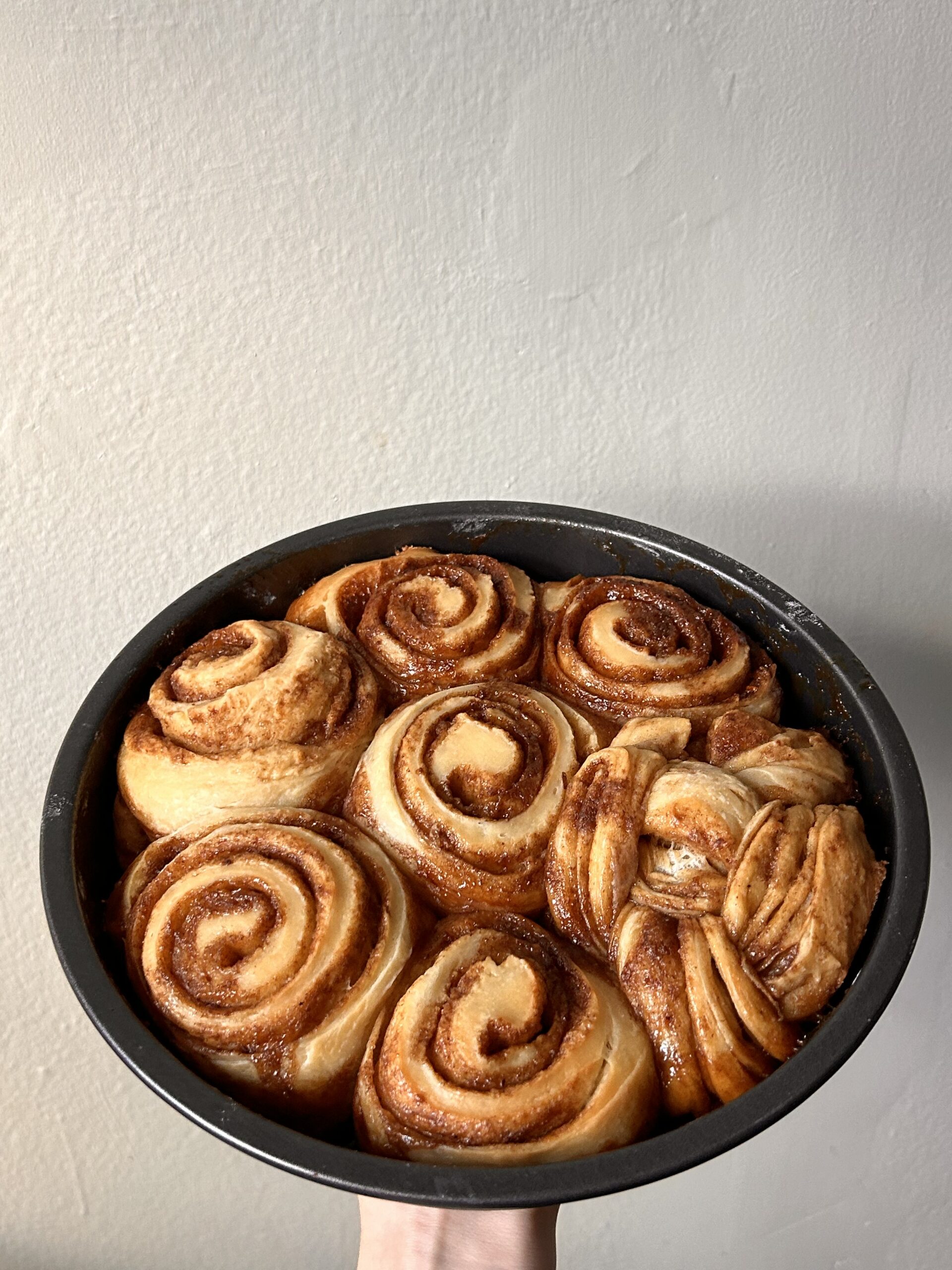 Freshly baked cinnamon rolls in a round pan, golden brown with caramelized edges.