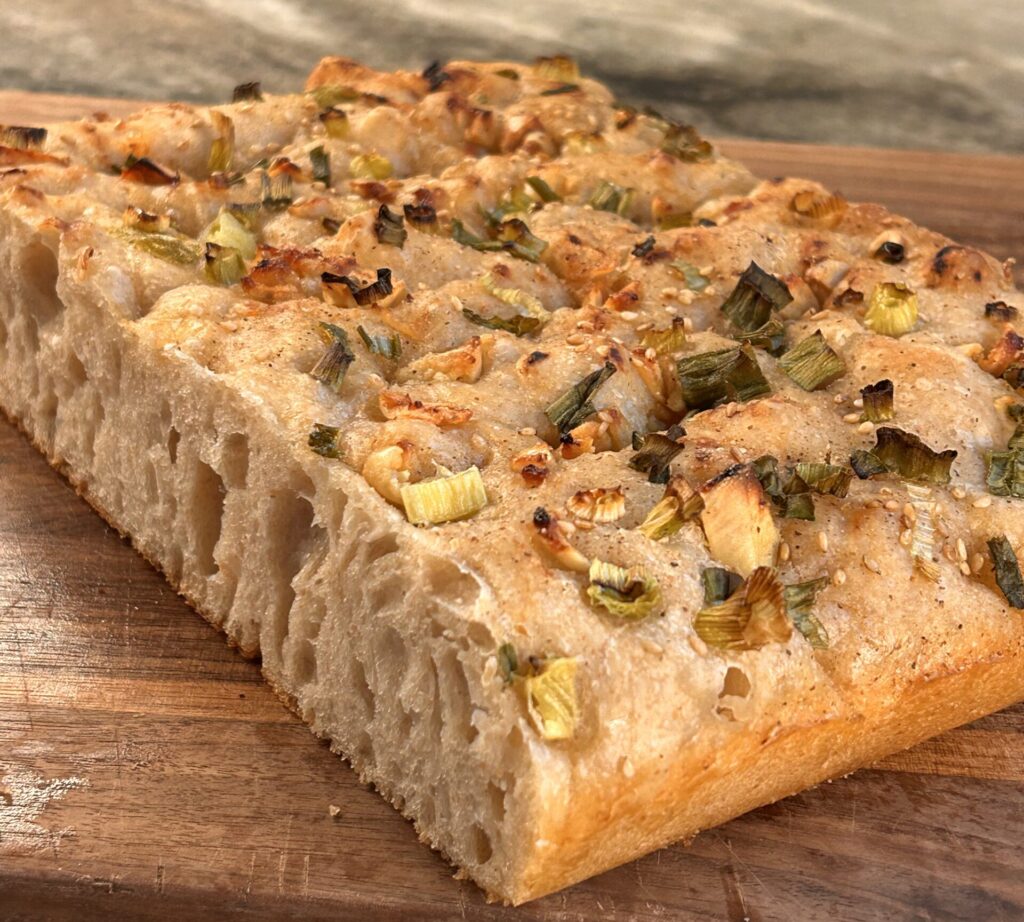 Close-up of freshly seasoned focaccia topped with scallions, sesame seeds, garlic, and miso paste.