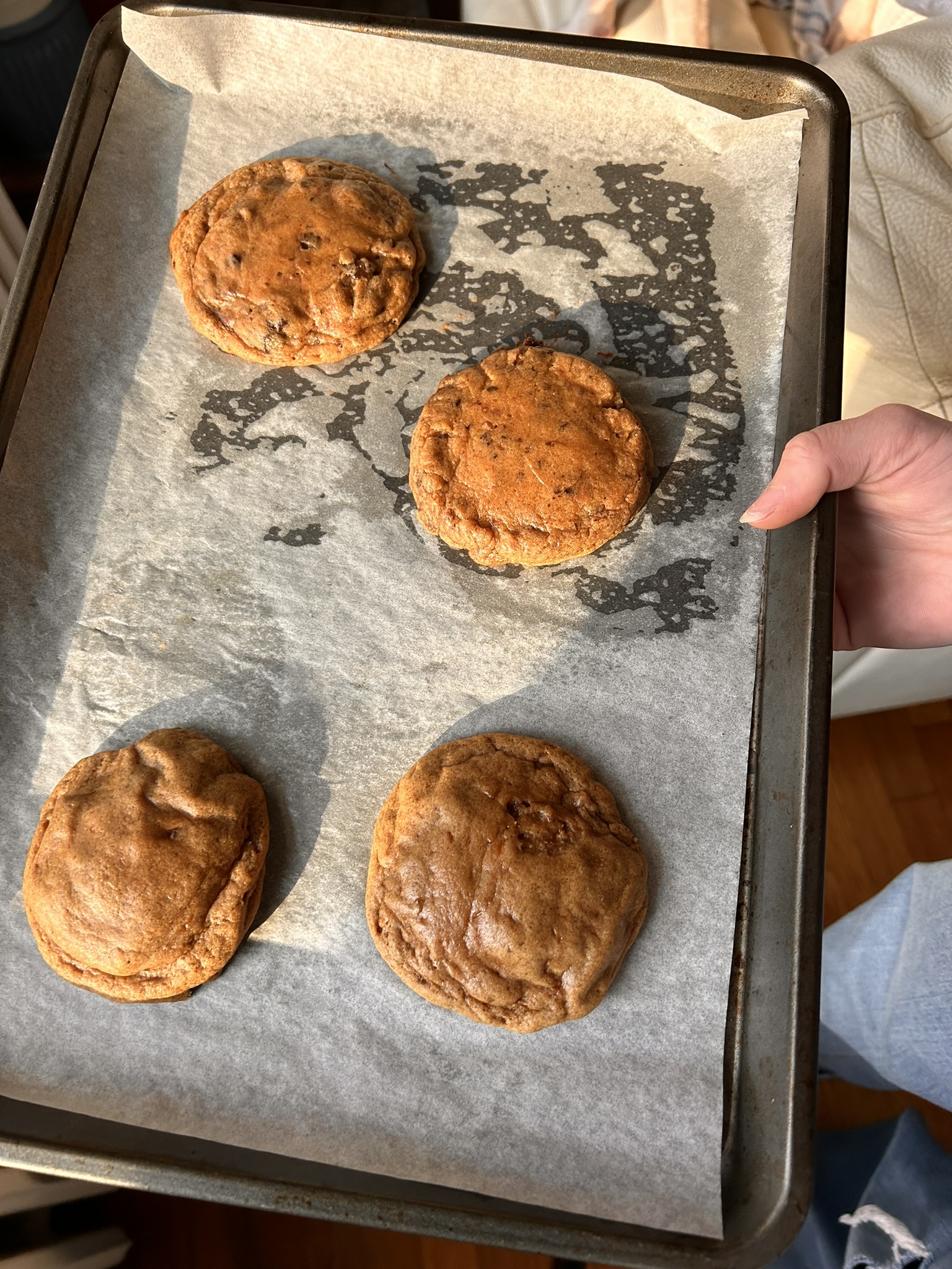 A tray of freshly baked burnt sugar ginger cookies on parchment paper, with warm golden-brown tops glistening in natural light