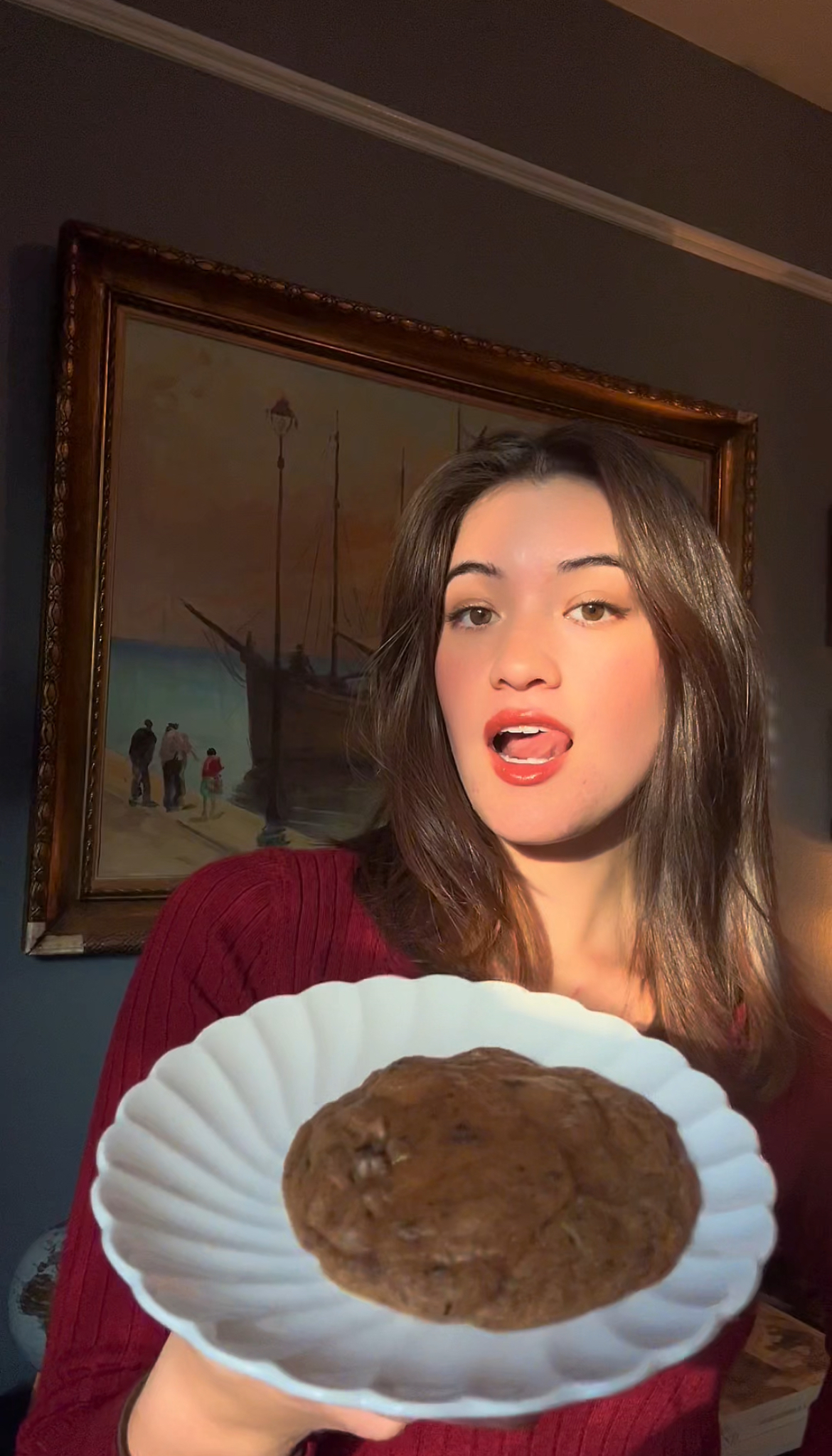 A smiling woman holding a white plate with a freshly baked brown butter miso chocolate chunk cookie, showcasing its golden-brown texture and chocolate chunks.