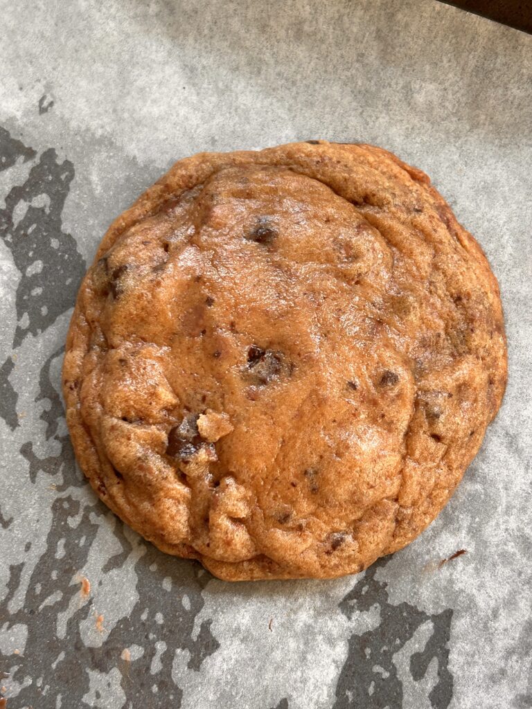 Close-up image of a freshly baked brown butter miso chocolate chunk cookie with golden edges and visible chocolate chunks.