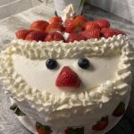 A Christmas strawberry shortcake with layers of light yellow sponge cake, fluffy whipped cream, and glossy red strawberries. Garnished with additional strawberry slices and whipped cream on top, the dessert’s red and white colors look especially festive for the holiday table.