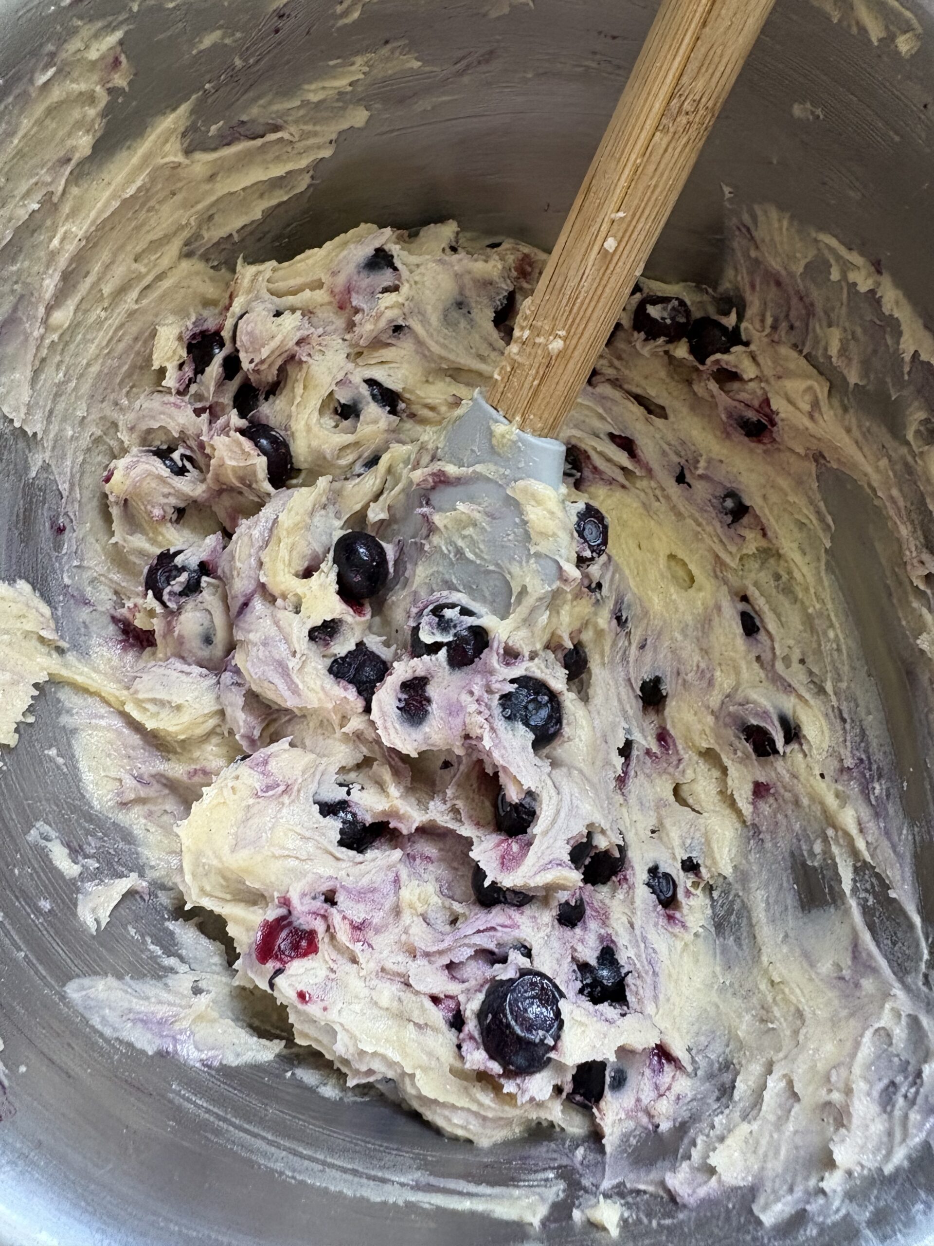 Blueberry muffin batter in mixing bowl . Thick blueberry muffin batter in a large stainless steel mixing bowl with a spatula
